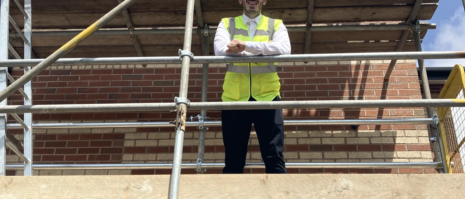 A person in hi-vis and a hard hat inspecting scaffolding at a brick building