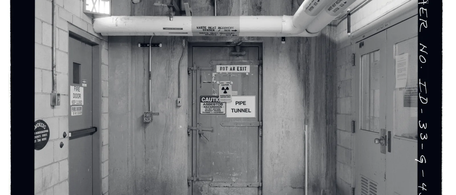 An archival photograph of a fire door beside a pipe penetrating a compartment wall