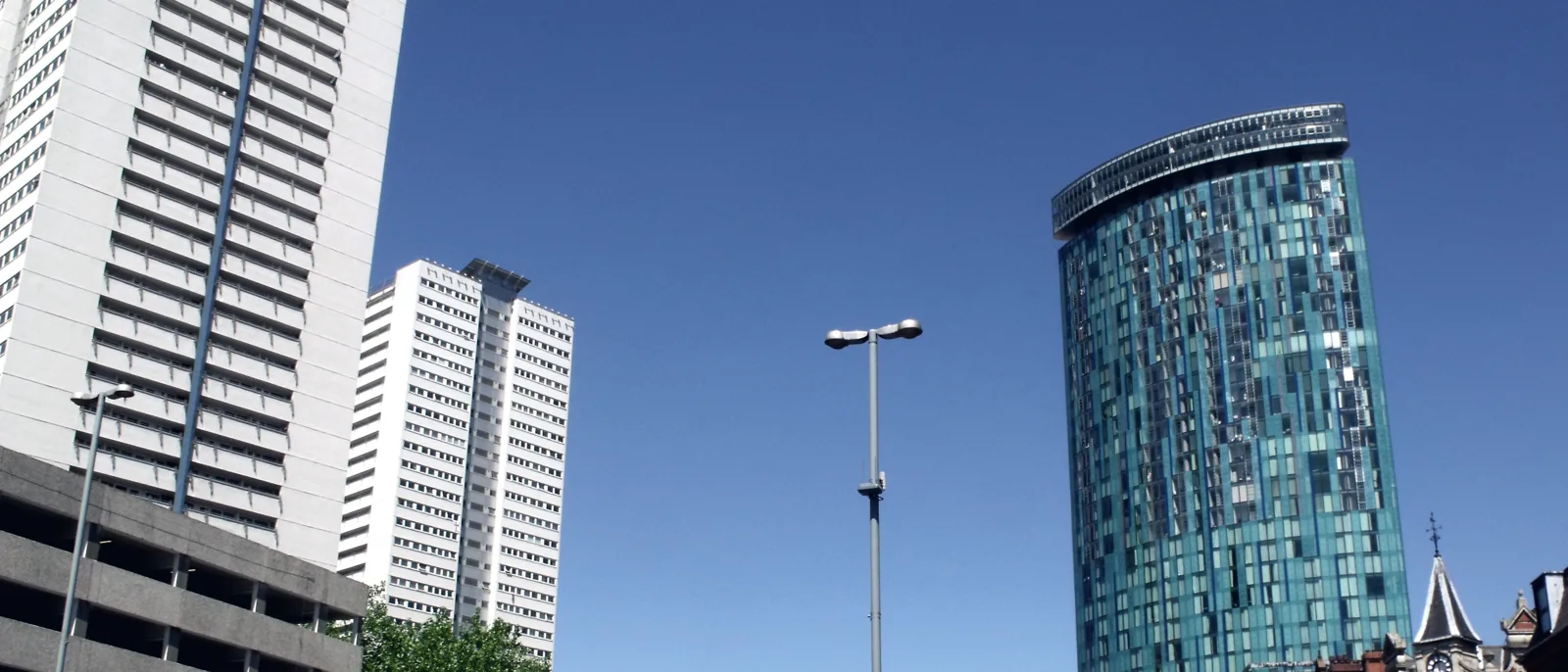 A pale twentieth-century residential tower block standing beside a green-glass clad tower against a clear sky