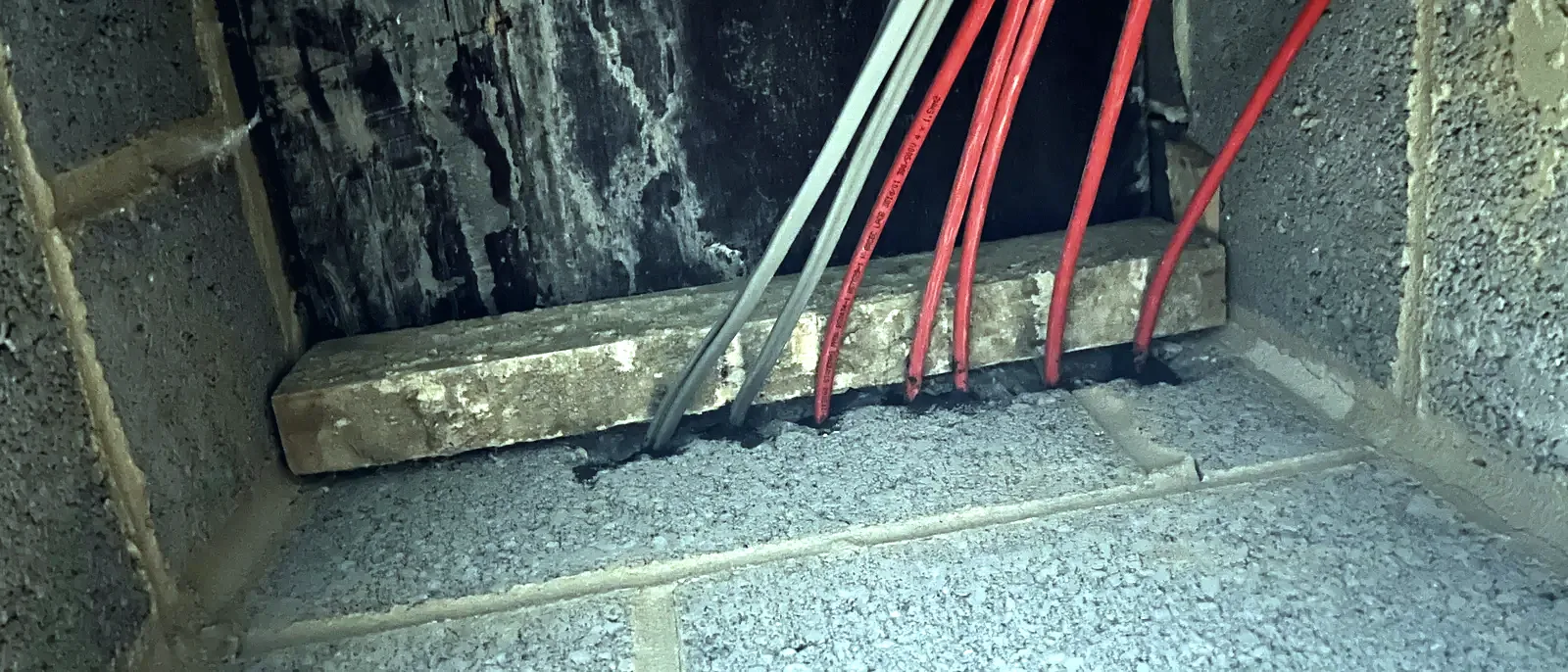 Pipework and cabling passing through masonry in a roof void, sealed around with red fire-stopping compound