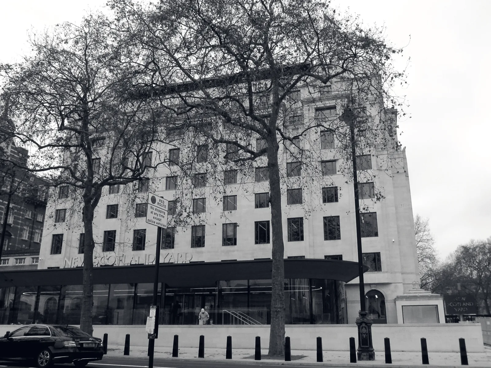 The Portland stone facade of a large civic police headquarters building behind mature plane trees