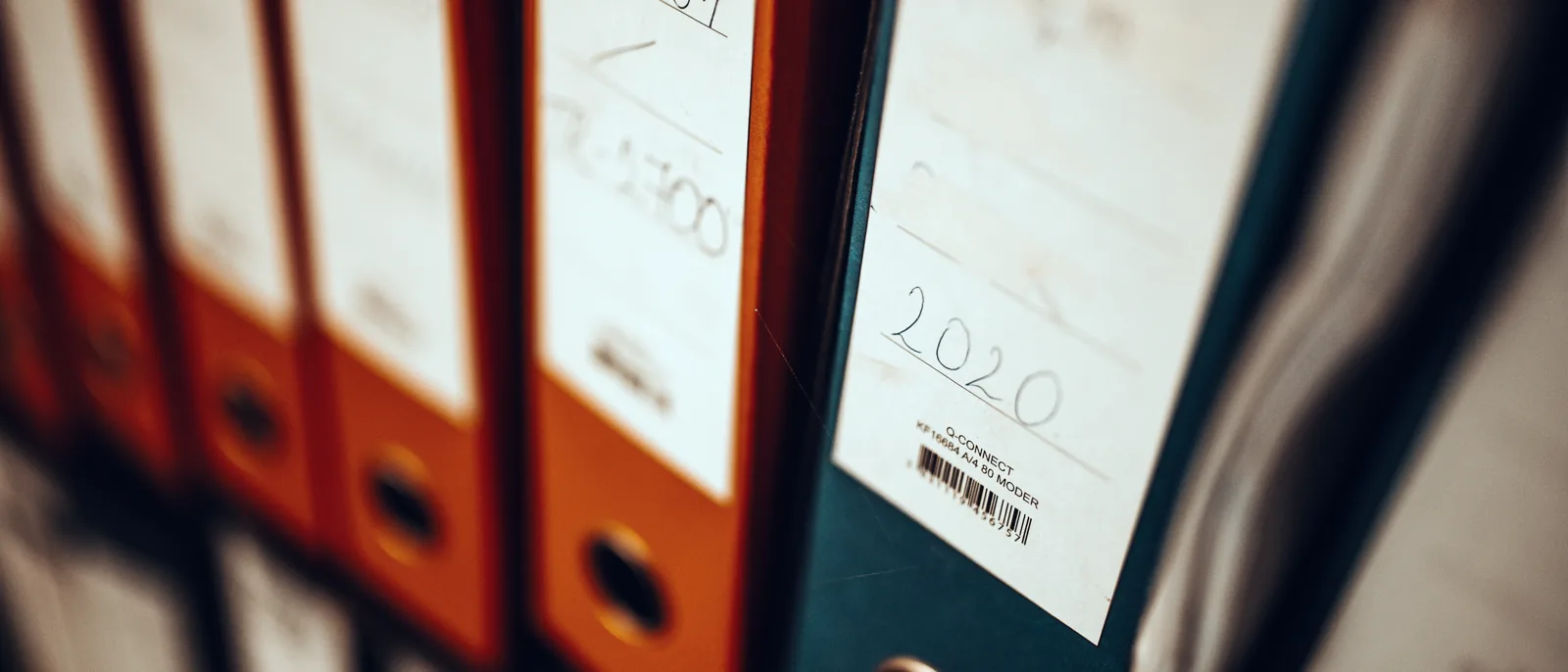 Lever-arch files with handwritten labels, side by side on an office shelf